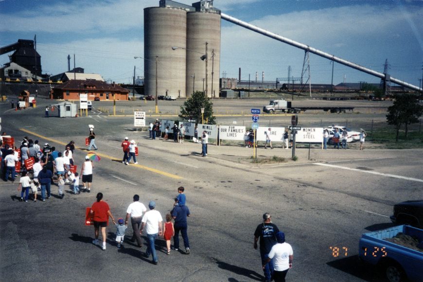 A birds-eye view of a protest in front of the Steel Mill. The mill's stacks are visible behind.