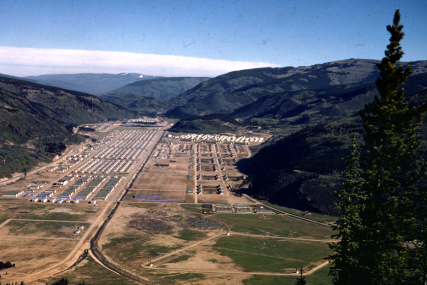 Overhead view of Camp Hale and its many barracks in summer. There is an evergreen tree in the foreground.