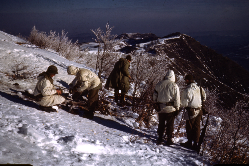 A group of soldiers standing on the side of a snowy mountain with dead bushes.