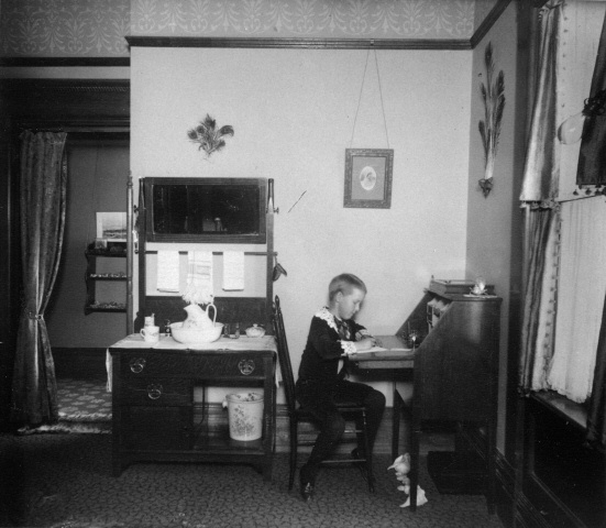 Child writing at desk, 1890-1900