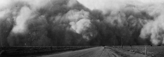 A black and white photo depicts a cloud of dust over a barren field. 