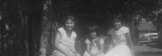 Black and white photo of 3 women in the 1950s. Two adult women in dresses pose with a young girl.