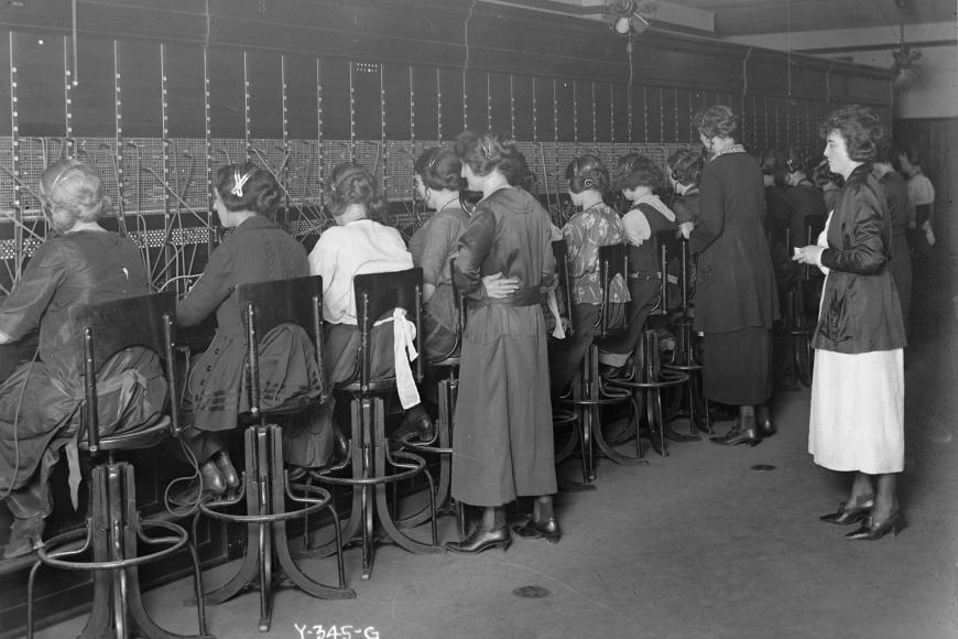 Teachers stand behind a group of students working at a switchboard