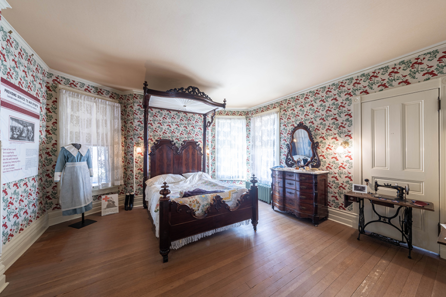 Master bedroom at the Center for Colorado Women's History. There's an ornate wooden frame bed, armoire, and ornate wallpaper. 
