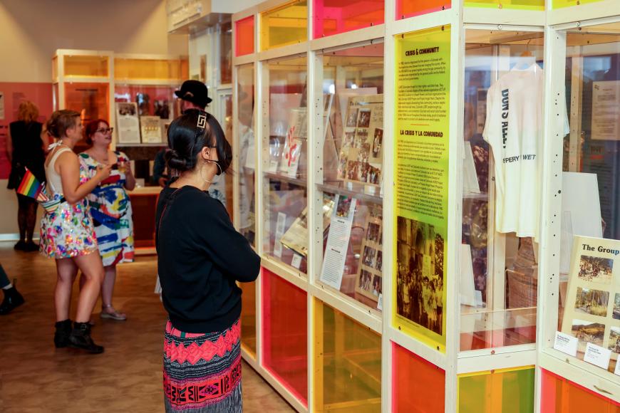 A woman looks at the multi-colored glass information and artifact cases making up Rainbows & Revolutions