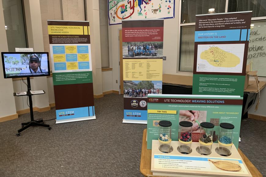 In the corner of a room, the Ute Stem Traveling Exhibit displays a Beadwork interactive, along with three pop-up banners and one touch screen video monitor playing an educational video on the Ute Mountain Ute Tribe.