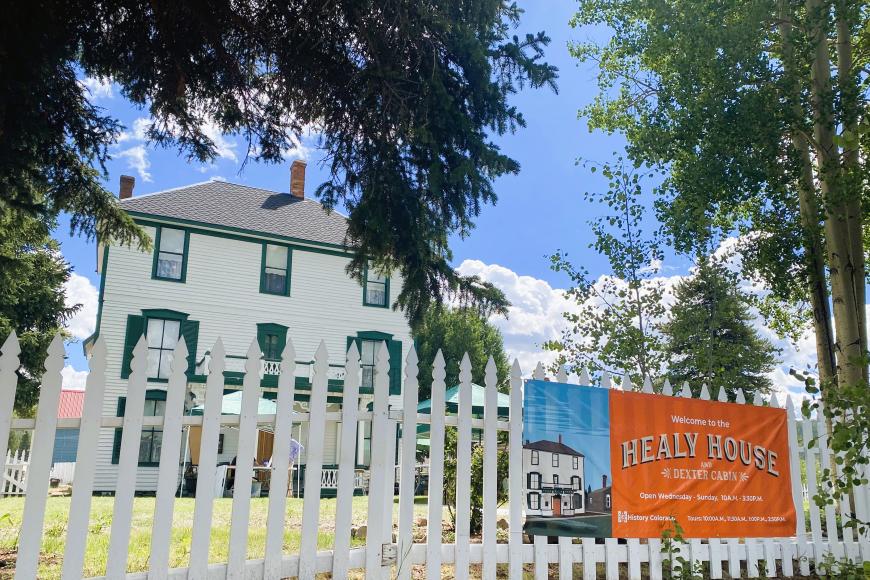 Exterior from fence of Healy House. There is a large orange banner outside showing opening hours.