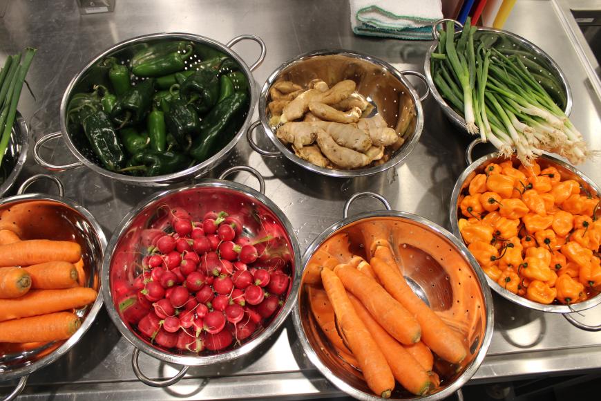 7 large bowls of fresh vegetables on a stainless steel table.