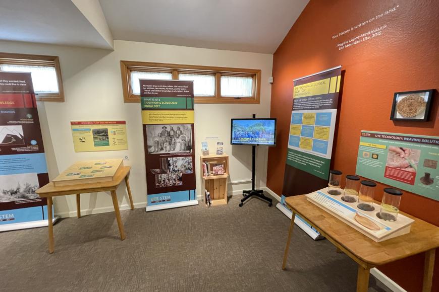 In the corner of a room, the Ute Stem Traveling Exhibit is displayed with three educational pop-up banners, two interactive Ute Knowledge displays, and one touch screen video monitor playing a video on the Ute Mountain Ute Tribe.