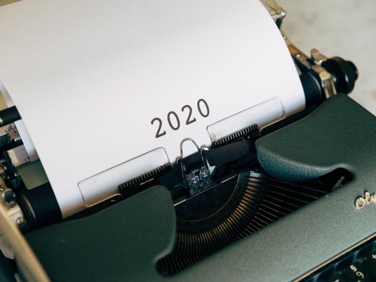 Photo of an old Olympic typewriter, with a piece of white typing paper in it, which simply says "2020" in large black numerals. 