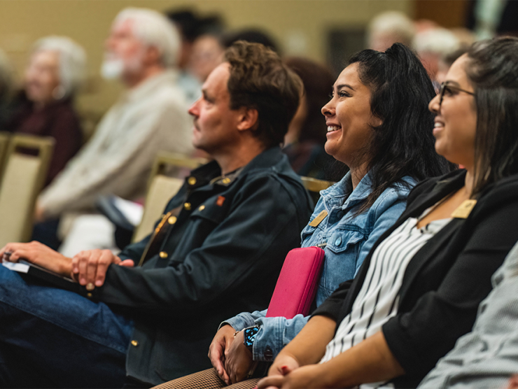 A diverse group of adults sit and smile while listening to a lecture at the History Colorado Center.