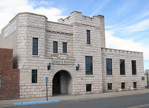 A picture of a building with white stone bricks with different sections and large arched entrance.